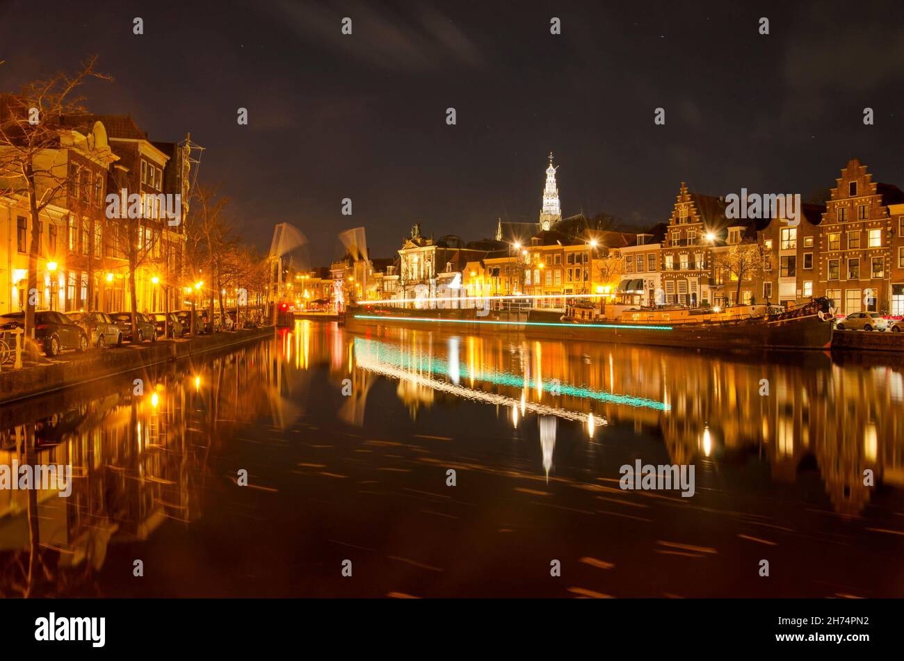 Haarlem, Paesi Bassi, 19 novembre 2021: Vista lungo il fiume Spaarne di notte con un percorso leggero di una barca che ha appena superato un ponte levatoio aperto Foto Stock