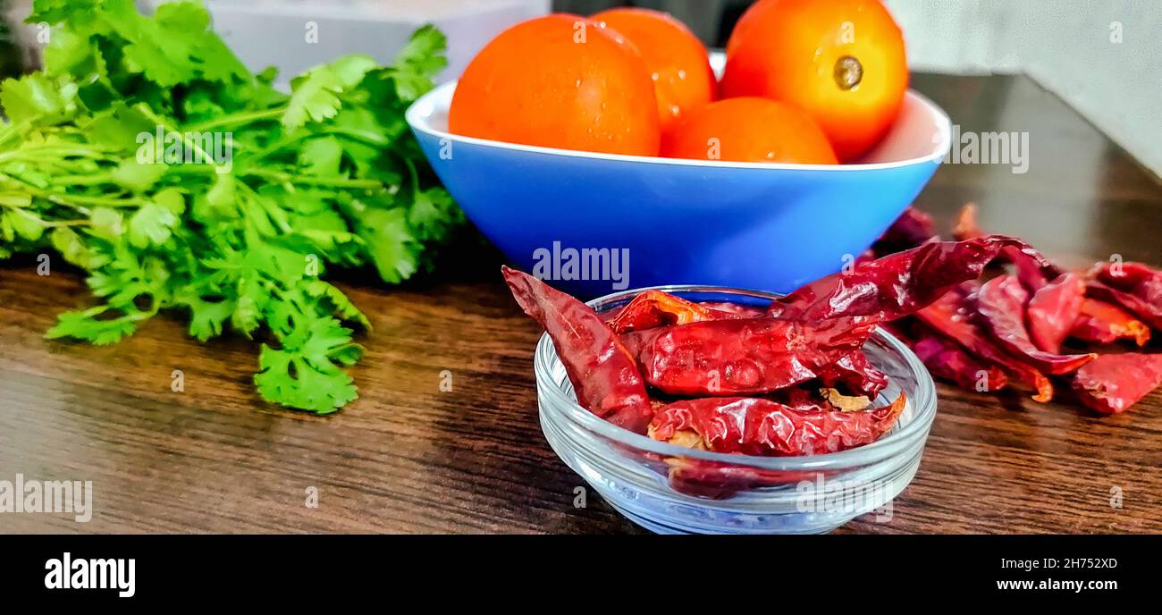 Alcune verdure, pomodori coriandolo e peperoncino rosso intero, per fare chutney e salsa su tavola di legno Foto Stock