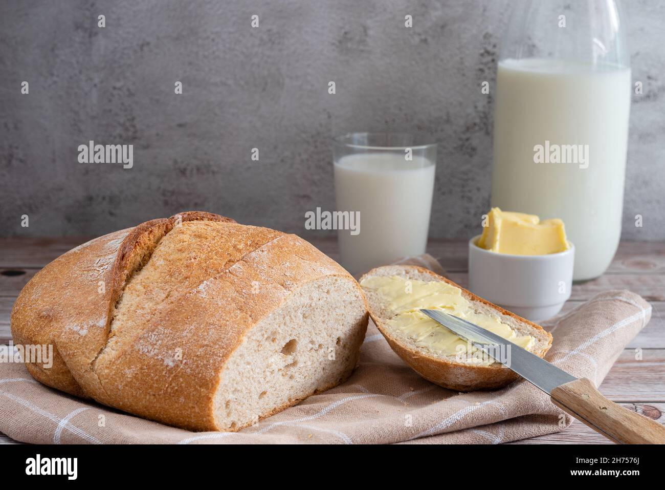 Pane fresco e burro fatto in casa su sfondo di legno. Il burro viene spalmato su un pezzo di pane. Foto Stock