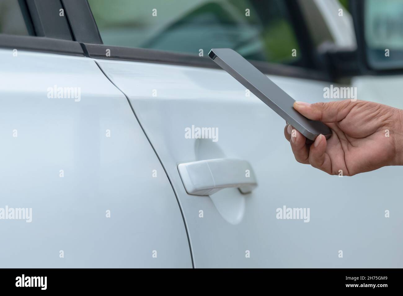 Mano di donna che tiene lo smartphone vicino alla porta dell'auto. Foto Stock