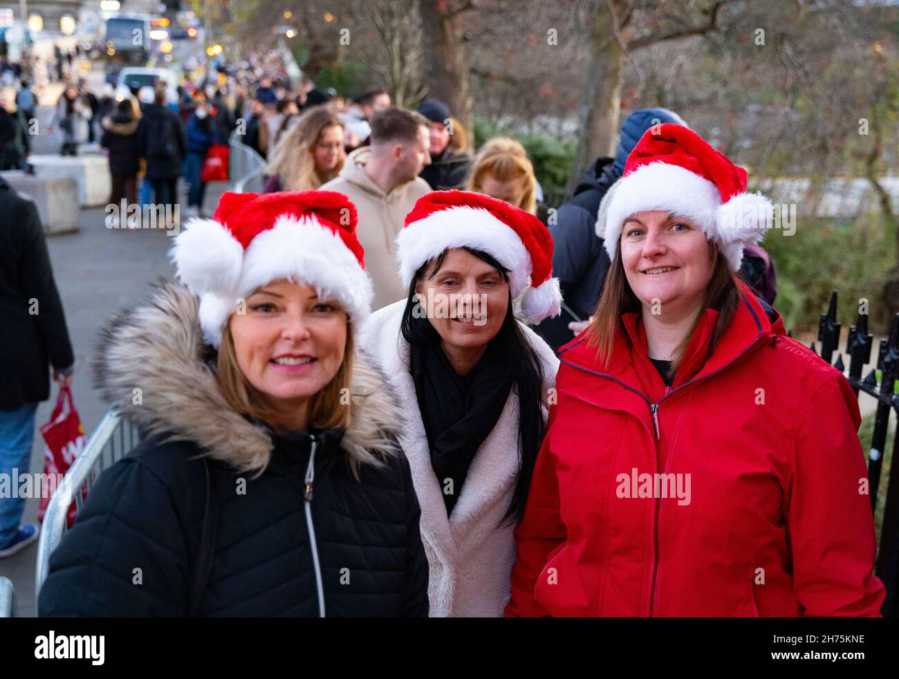 Edimburgo, Scozia, Regno Unito. 20 novembre 2021. Il giorno di apertura del tradizionale mercatino di Natale nei giardini di East Princes Street a Edimburgo ha visto migliaia di visitatori in fila per un massimo di 30 minuti per ottenere l'ingresso. Il mercato è molto più piccolo rispetto agli anni precedenti e il sovraffollamento era una preoccupazione. PIC; tre membri del pubblico in Santa Hats attendere nella lunga coda per entrare nel mercato. Iain Masterton/Alamy Live News. Foto Stock