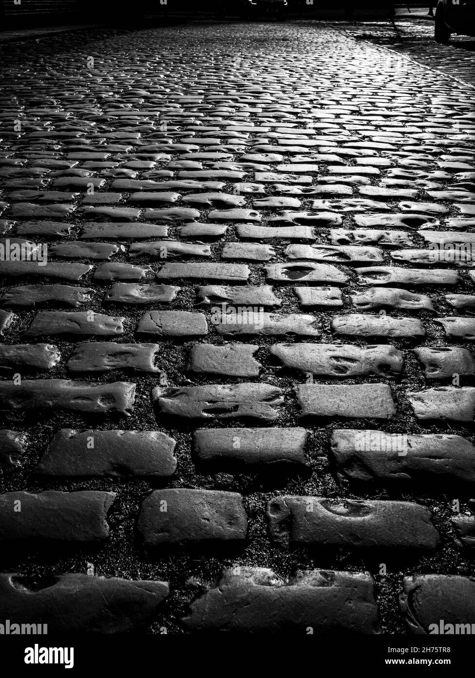 vista ravvicinata che si affaccia su vecchi ciottoli sulla strada in bianco e nero Foto Stock