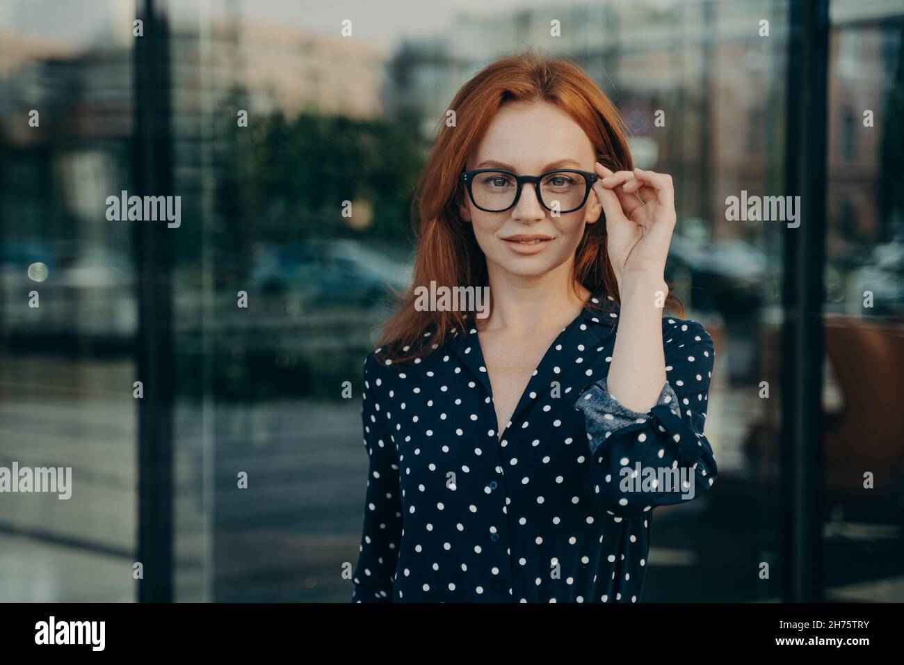 Bella donna rossa pone vicino ufficio edificio contro sfondo sfocato Foto Stock