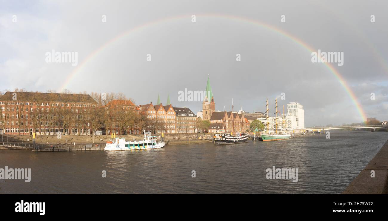 Panorama del centro storico di Brema, Germania sul fiume Weser con il sole che splende sullo Schlachte e un arcobaleno che copre il cielo Foto Stock