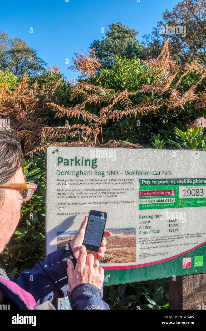 Donna che usa l'app RingGo sul suo telefono cellulare per pagare una tassa di parcheggio al parcheggio Dersingham Bog NNR a Wolferton. Foto Stock