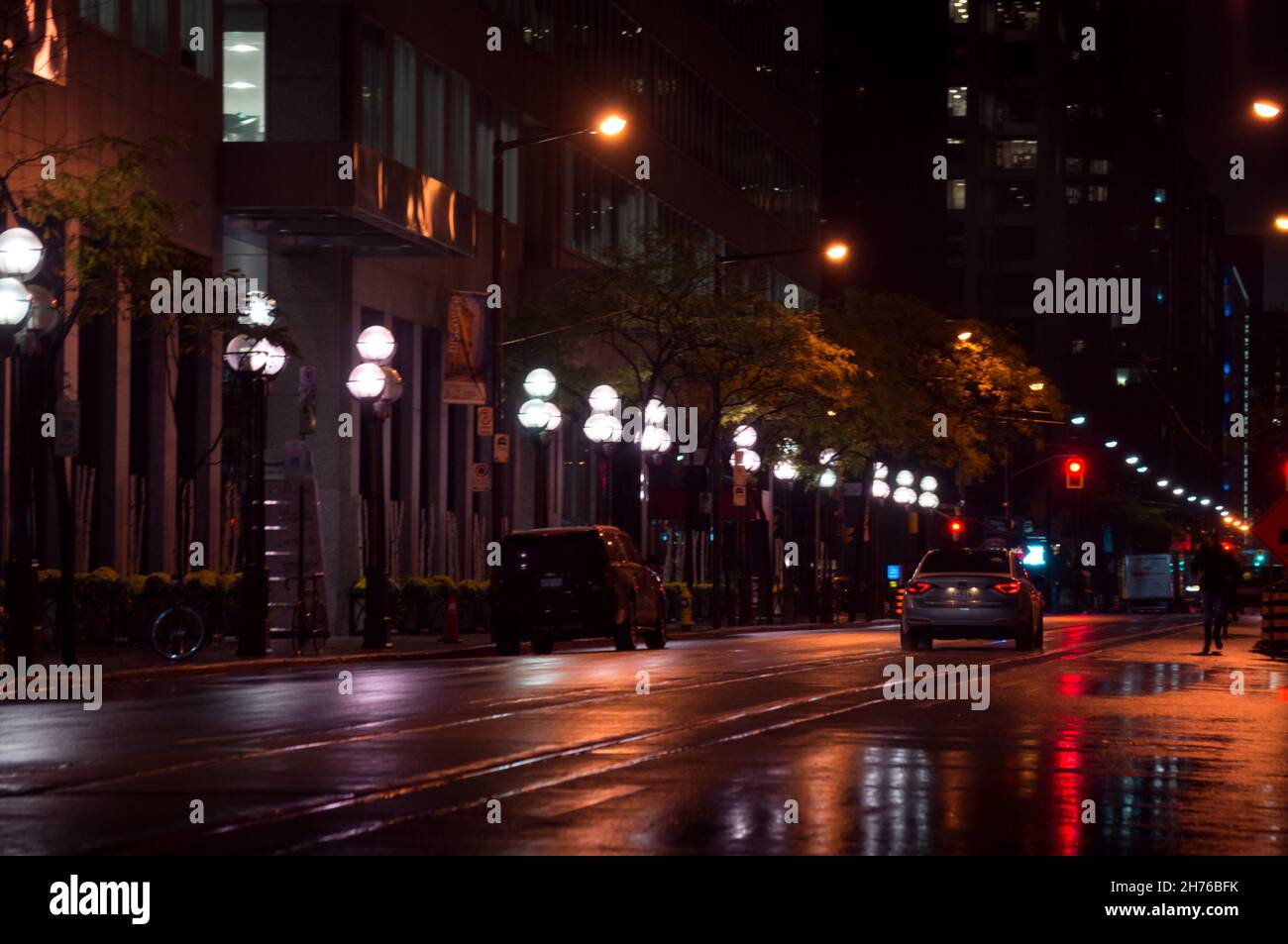 Toronto, Canada - 10 30 2021: Vista notturna piovosa lungo Wellington Street da Yonge Street nel centro di Toronto con una linea di streetlamps, automobili Foto Stock