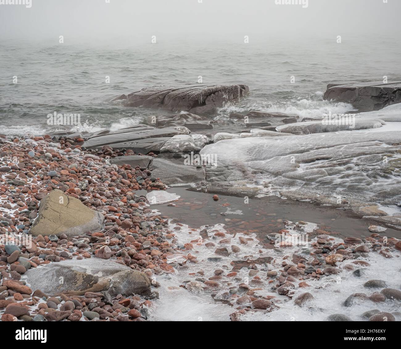 Rocce ricoperte di ghiaccio e acqua ghiacciata lungo la riva di un lago settentrionale in inverno Foto Stock