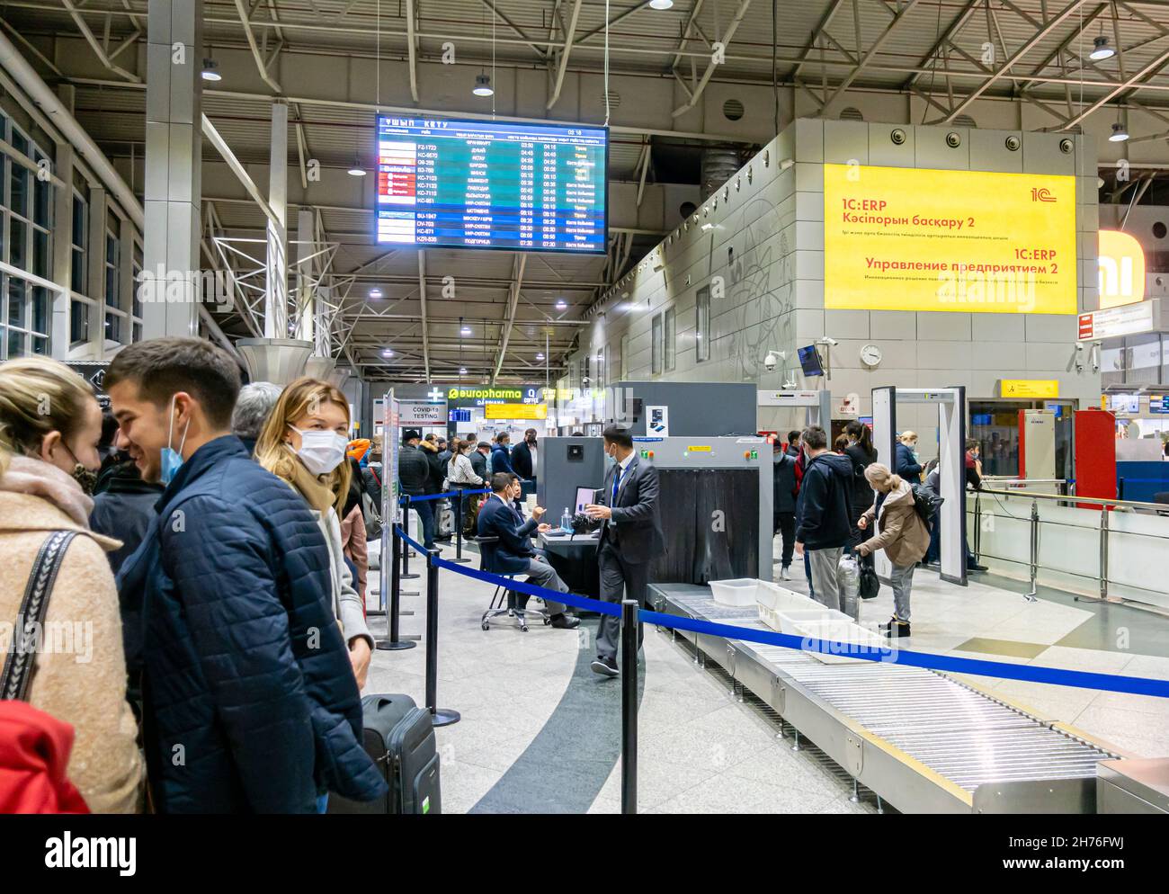 I passeggeri in maschere facciali in attesa in coda forsSacchi bagagli di sicurezza si trovano all'ingresso del terminal dell'aeroporto di Almaty, Kazakhstan Foto Stock