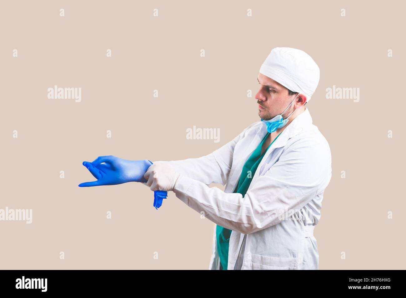 Giovane medico in tuta bianca e maschera protettiva per la respirazione mette i guanti sulle mani su sfondo giallo isolato. Foto Stock