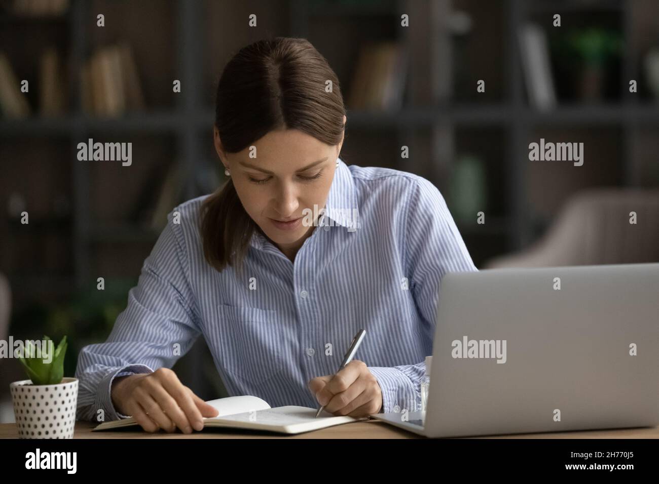 Donna millennial concentrata seduta alla scrivania jotting informazioni in notebook Foto Stock Donna millennial concentrata seduta alla scrivania jotting informazioni in notebook Foto Stock
