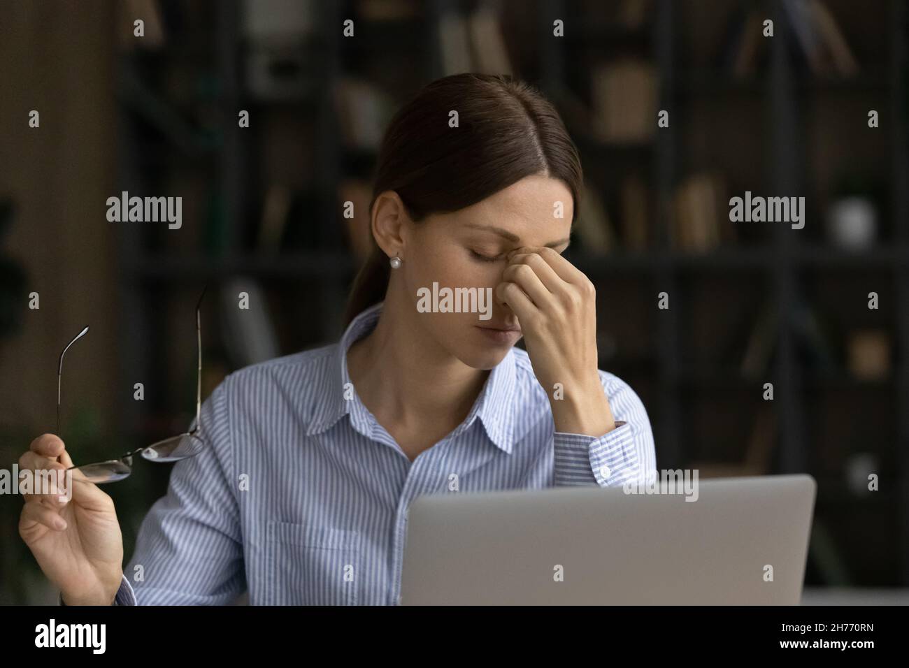 Una donna d'affari stanca toglie gli occhiali massaggiando il ponte nasale Foto Stock