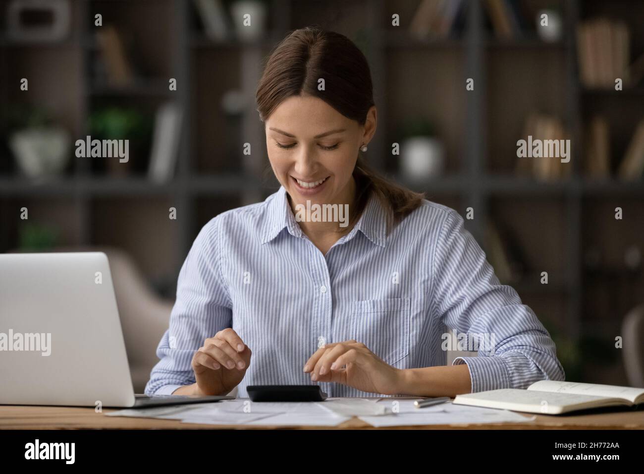 La donna attraente si siede alla scrivania contando il budget personale, effettua calcoli Foto Stock