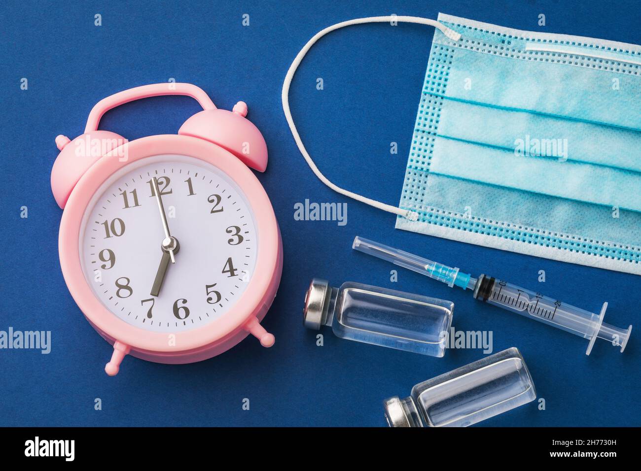 Sveglia e farmaci su sfondo blu, concetto tempo di vaccinare Foto Stock