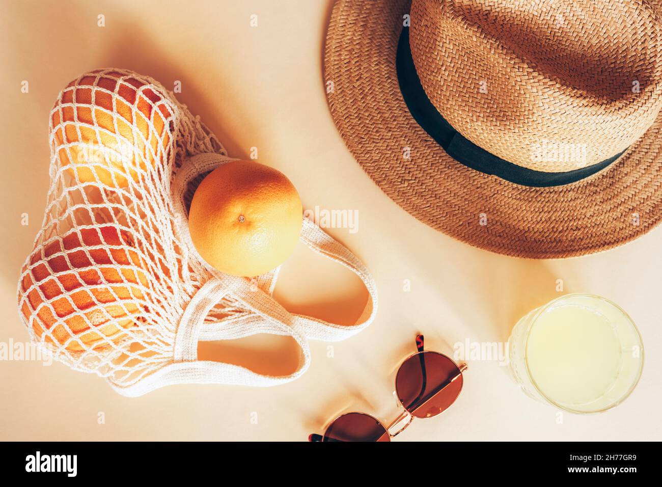 Arance in una borsa a corda, vetro con limonata, cappello da spiaggia e occhiali da sole su sfondo chiaro, vista dall'alto, piatto. Foto Stock