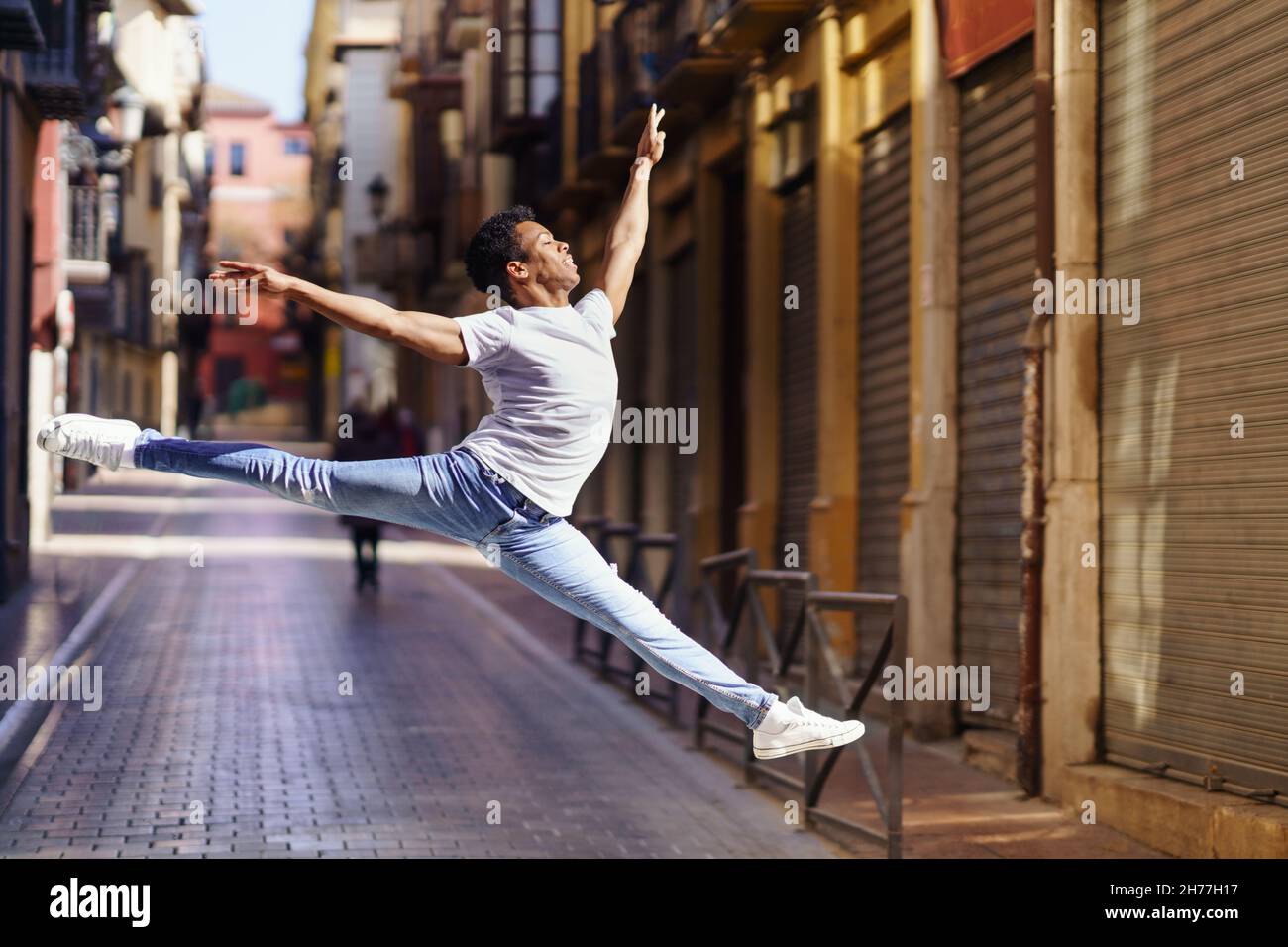 Giovane uomo nero che fa un salto acrobatico nel mezzo della strada. Foto Stock