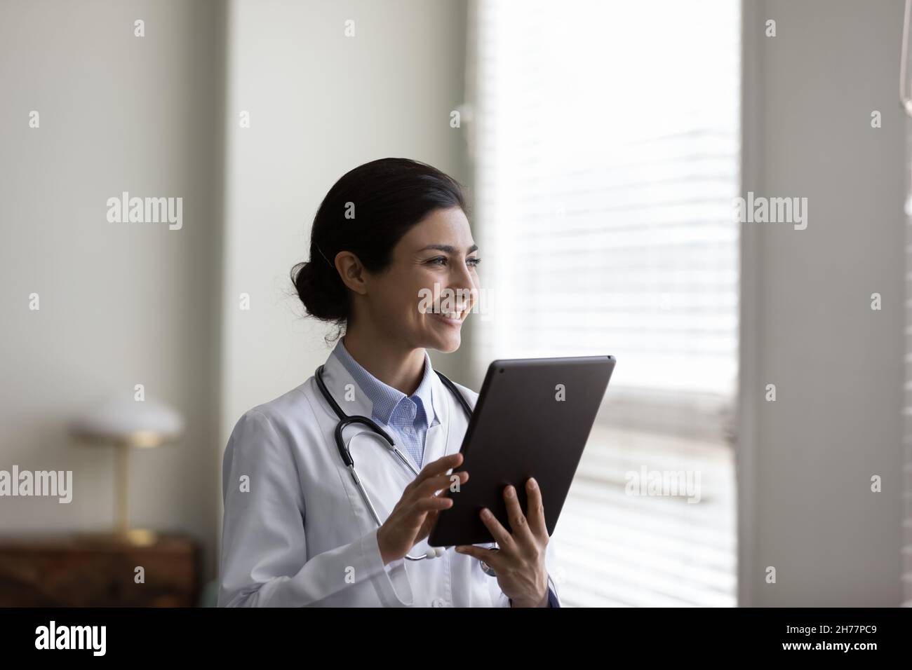 Sorridente sognante giovane donna indiana medico in mano tablet Foto Stock