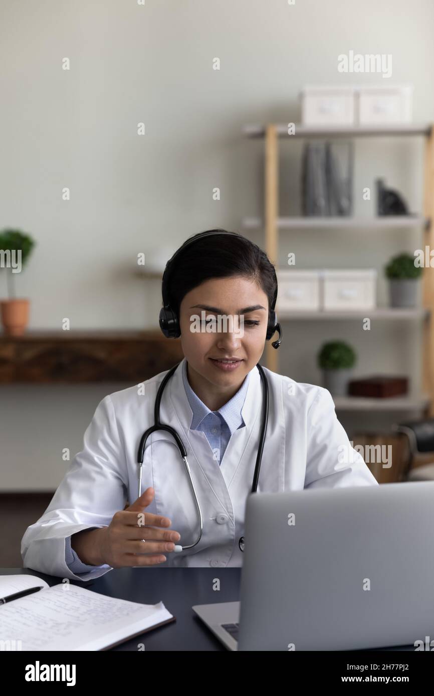 Foto verticale medico indiano in cuffie parlare, utilizzando il computer portatile Foto Stock