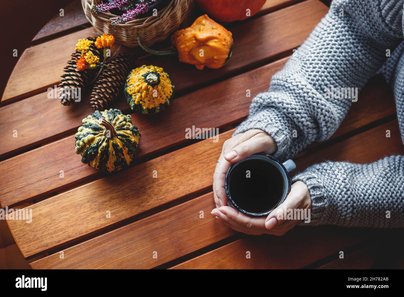 Gusta un forte caffè nero. Donna tenuta tazza di bevanda calda in casa accogliente interno con decorazione autunno. Tavolo in legno Foto Stock