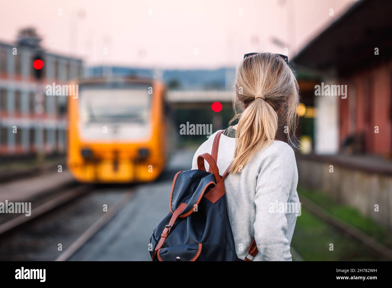 Viaggiatore solo che guarda arrivare in treno alla stazione ferroviaria. Treno passeggeri in città. La donna viaggia da sola Foto Stock