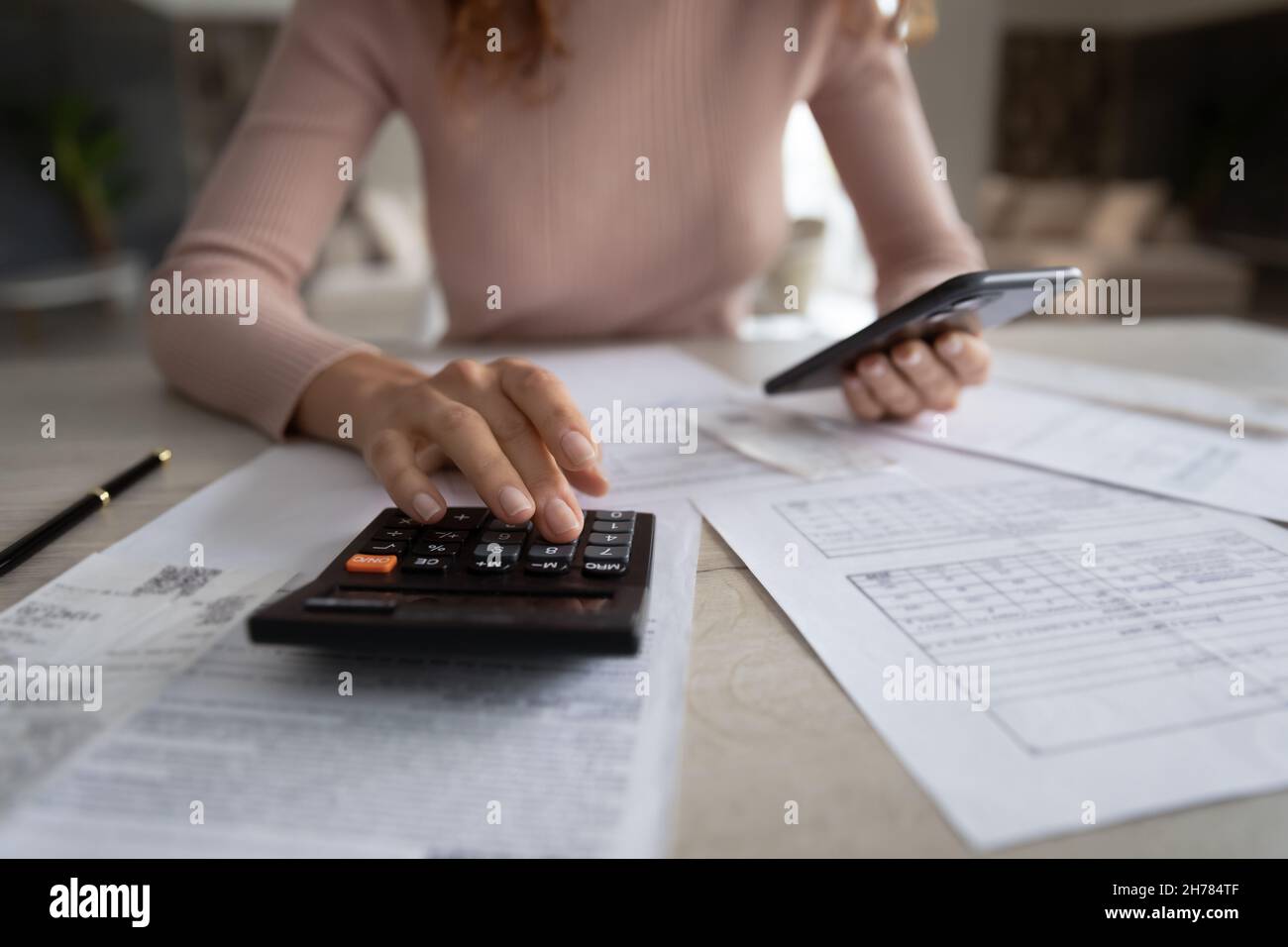 Primo piano donna calcolo fatture, utilizzando calcolatrice e smartphone Foto Stock