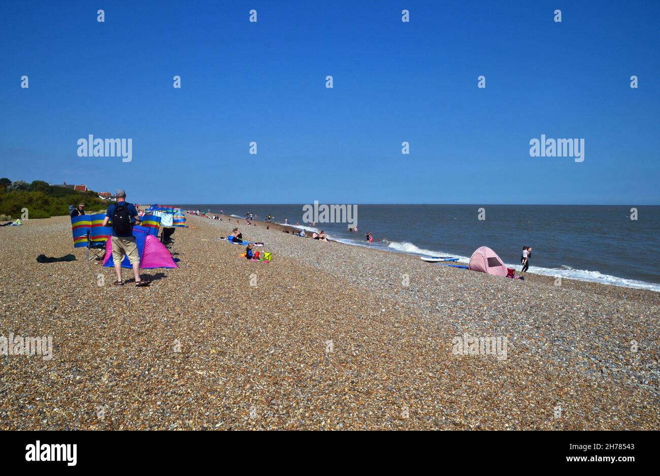 Le persone che si godono la spiaggia di ciottoli in una giornata di sole luminoso nel mese di agosto. Thorpeness, Suffolk, Regno Unito Foto Stock