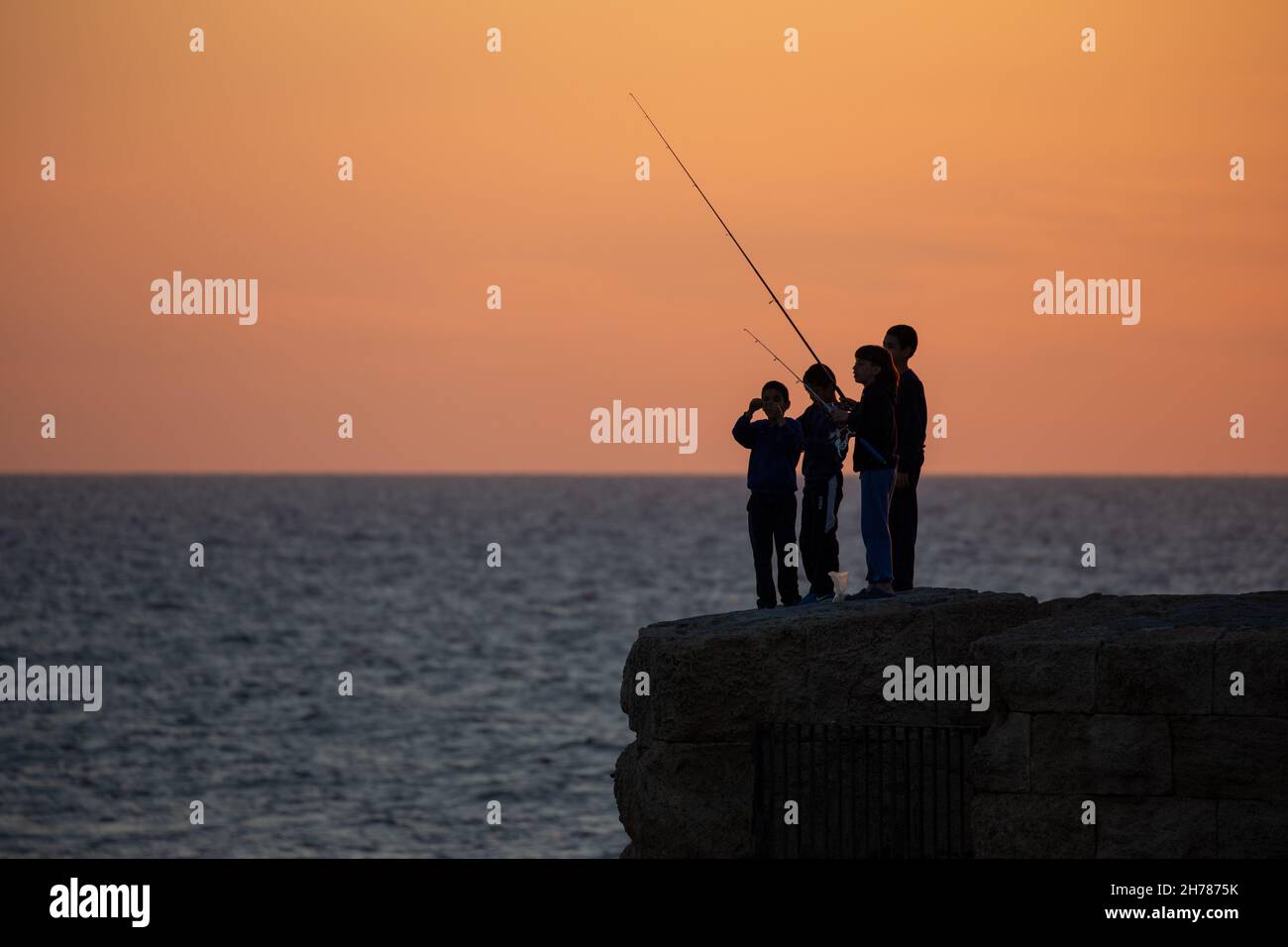 Tramonto mediterraneo fotografato alla silhouette di Acre Israel di pesca ragazzi locali Foto Stock