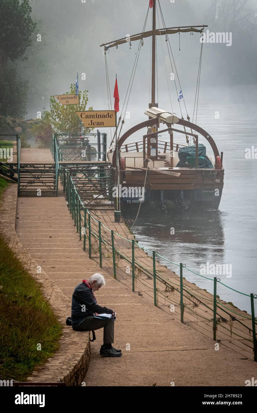Uomo che legge in attesa della barca turistica la Roque-Gageac, coperta. La Dordogna. Francia. Ottobre 2021 Foto Stock