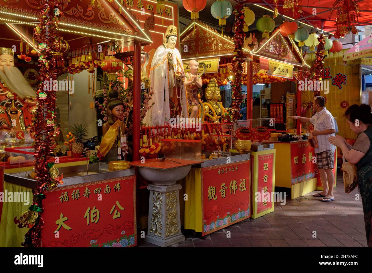 Adoratori ai santuari di preghiera taoisti e indù allestiti di fronte ad un negozio di paraphernalia religiosa buddista; Waterloo Street, Bugis, Singapore Foto Stock
