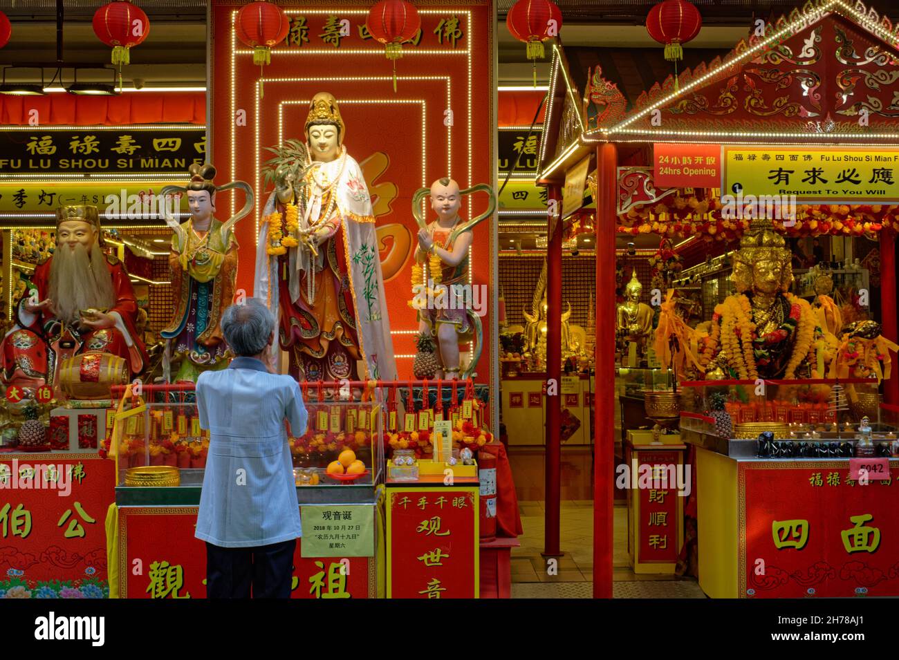 Un adoratore ai santuari di preghiera taoisti e indù allestito di fronte ad un negozio di paraphernalia religiosa buddista; Waterloo Street, Bugis, Singapore Foto Stock