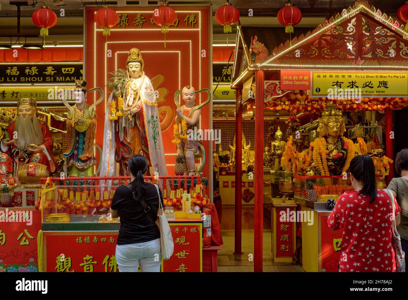 Adoratori ai santuari di preghiera taoisti e indù allestiti di fronte ad un negozio di paraphernalia religiosa buddista; Waterloo Street, Bugis, Singapore Foto Stock