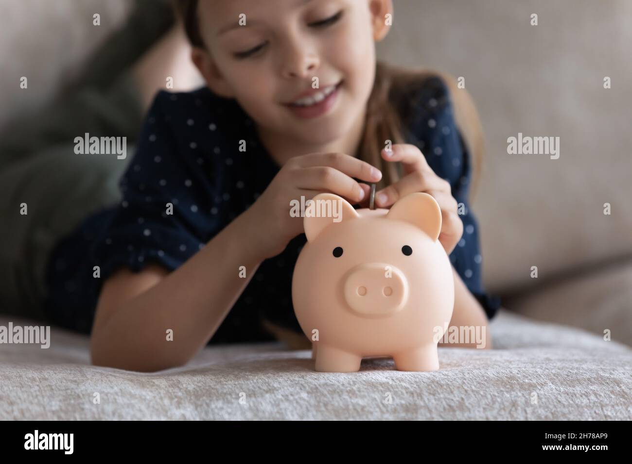 Bambina sdraiata sul divano mettere la moneta in una banca di maialino Foto Stock
