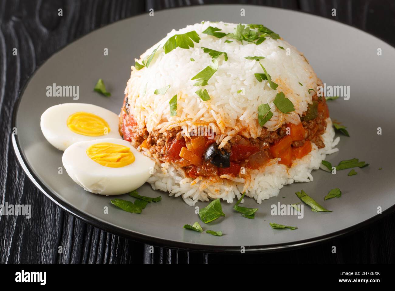 Il gustoso tapado Arroz è un piatto peruviano composto da riso, verdure, manzo macinato e uova bollite in primo piano nel piatto sul tavolo. Orizzontale Foto Stock
