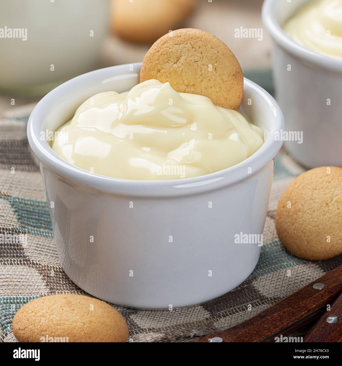 Primo piano di budino cremoso alla vaniglia in una tazza bianca con cialde alla vaniglia su un tovagliolo di stoffa Foto Stock