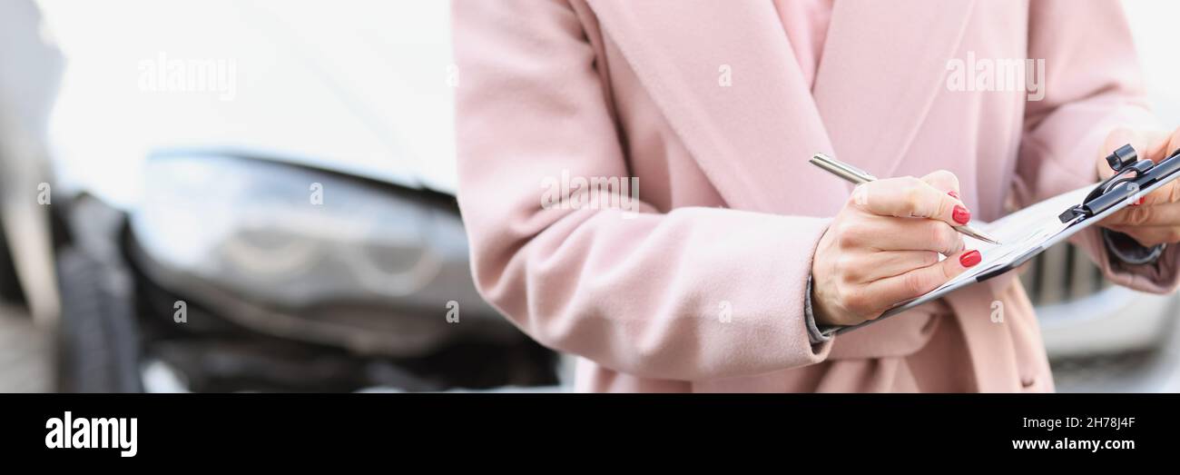 Donna in cappotto che compila i documenti sullo sfondo di auto rotto closeup Foto Stock