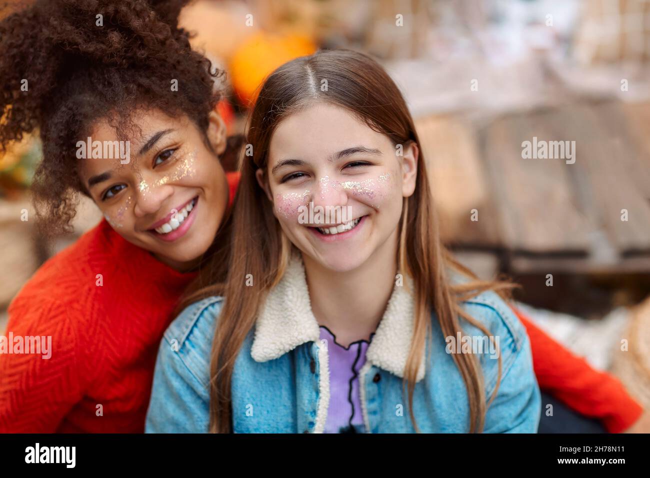 Ritratto di due allegre fidanzate multirazziale sorridenti alla macchina fotografica mentre trascorrono del tempo nella natura autunnale, allegre ragazze teen di razze diverse godendo wa Foto Stock