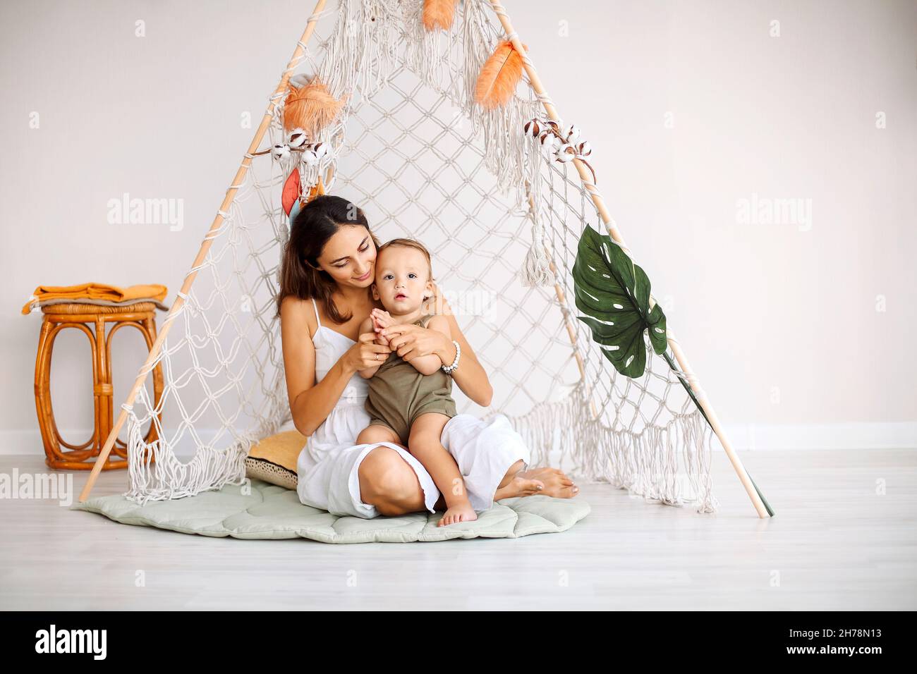 Giovane famiglia felice amorevole madre con bambino seduto insieme in wigwam teepee a casa, mamma giocando con bambino in tenda di gioco, scatto orizzontale. MOTH Foto Stock