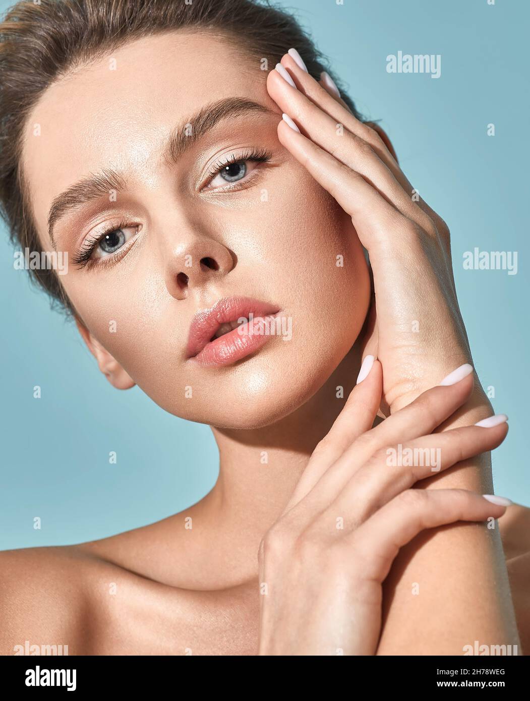 Cura della pelle. Bella donna con pelle sana del viso che tocca la sua pelle idratata del viso, su sfondo blu. Alta qualità Foto Stock