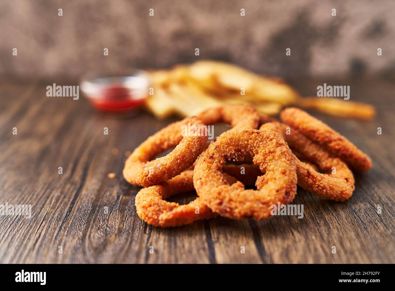 Mazzo di anelli di cipolla impanati e patatine fritte su una superficie di  legno Foto stock - Alamy