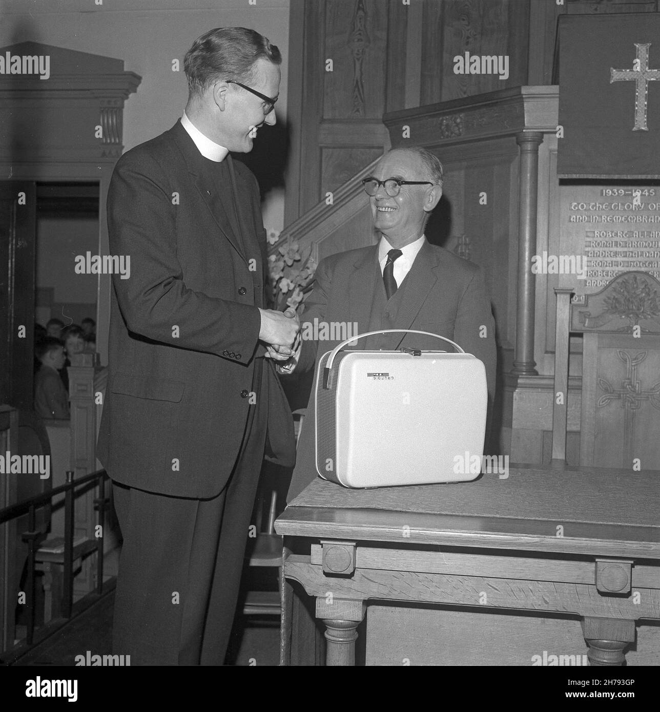 1965, storico, all'interno di una chiesa, un ministro anziano scuotendo le mani di un anziano guardiano della chiesa e presentandolo con un regalo, un registratore portatile a nastro, St Andrews, Fife, Scozia, Regno Unito. Foto Stock