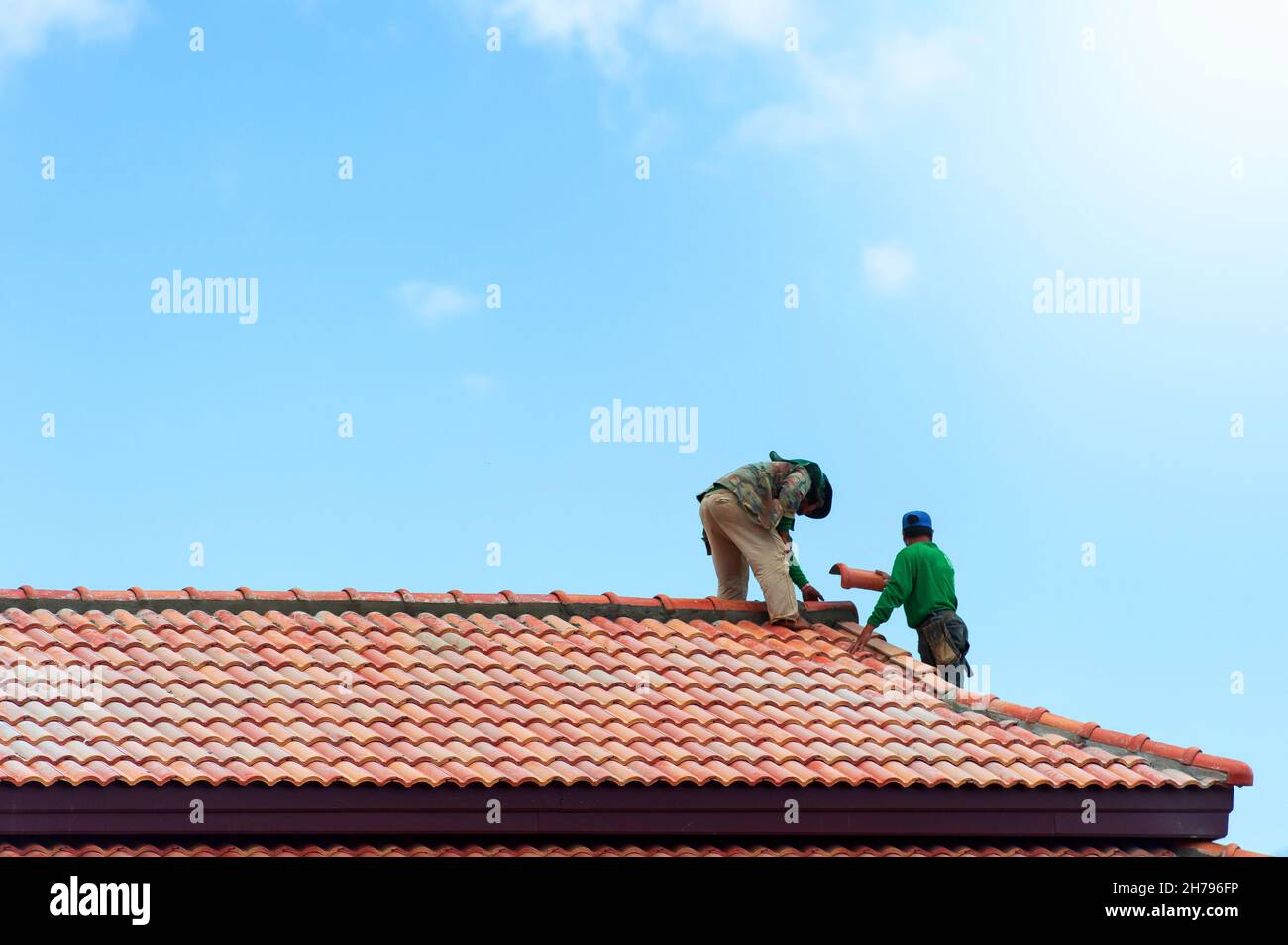 Due costruttori asiatici che installano le tegole sul tetto in costruzione. Costruzione di tetti. Foto Stock