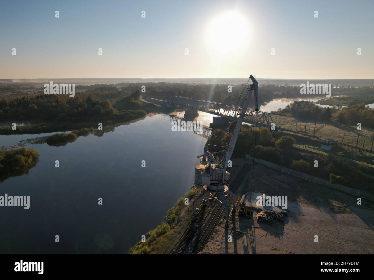 Gru portuale inattiva sullo sfondo di un fiume e di un ponte ferroviario all'alba. Foto Stock