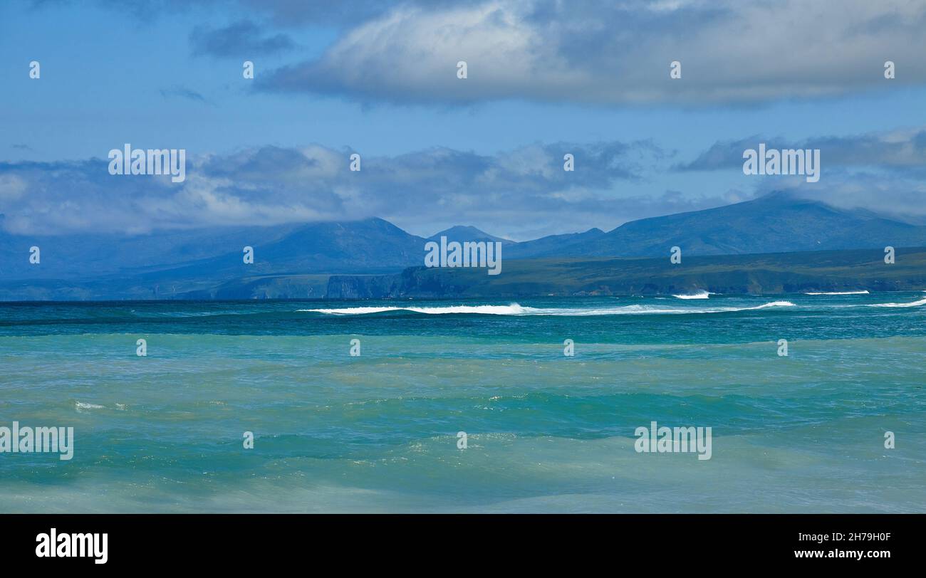 Acqua di smeraldo del mare di Okhotsk sullo sfondo di un ridgeo vulcanico di montagna sull'isola Iturup territori disputati tra la Russia e il Giappone. Foto Stock