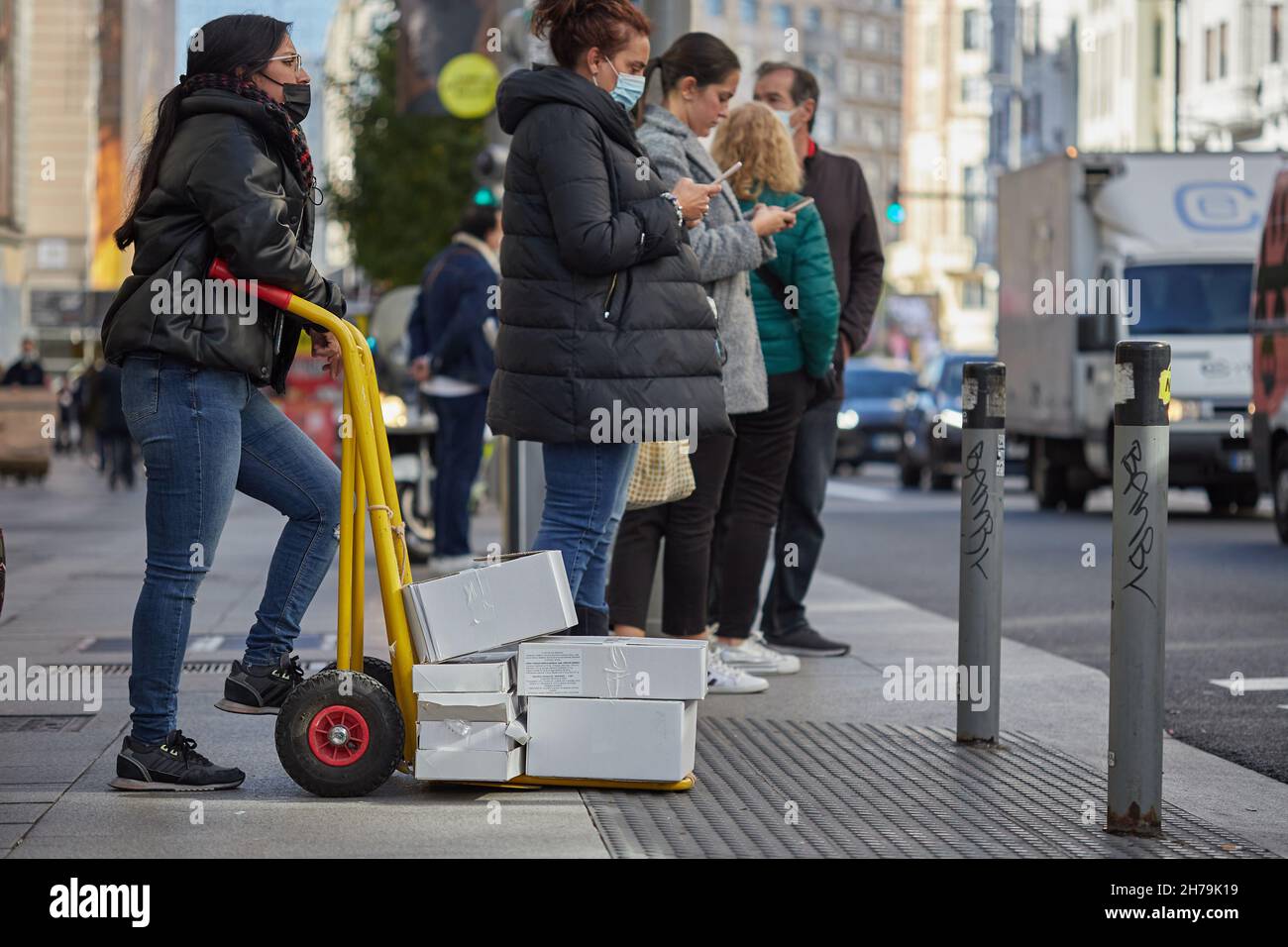 Consegna pacchi donna in attesa in un marciapiede in Gran Via (Madrid, Spagna) Foto Stock