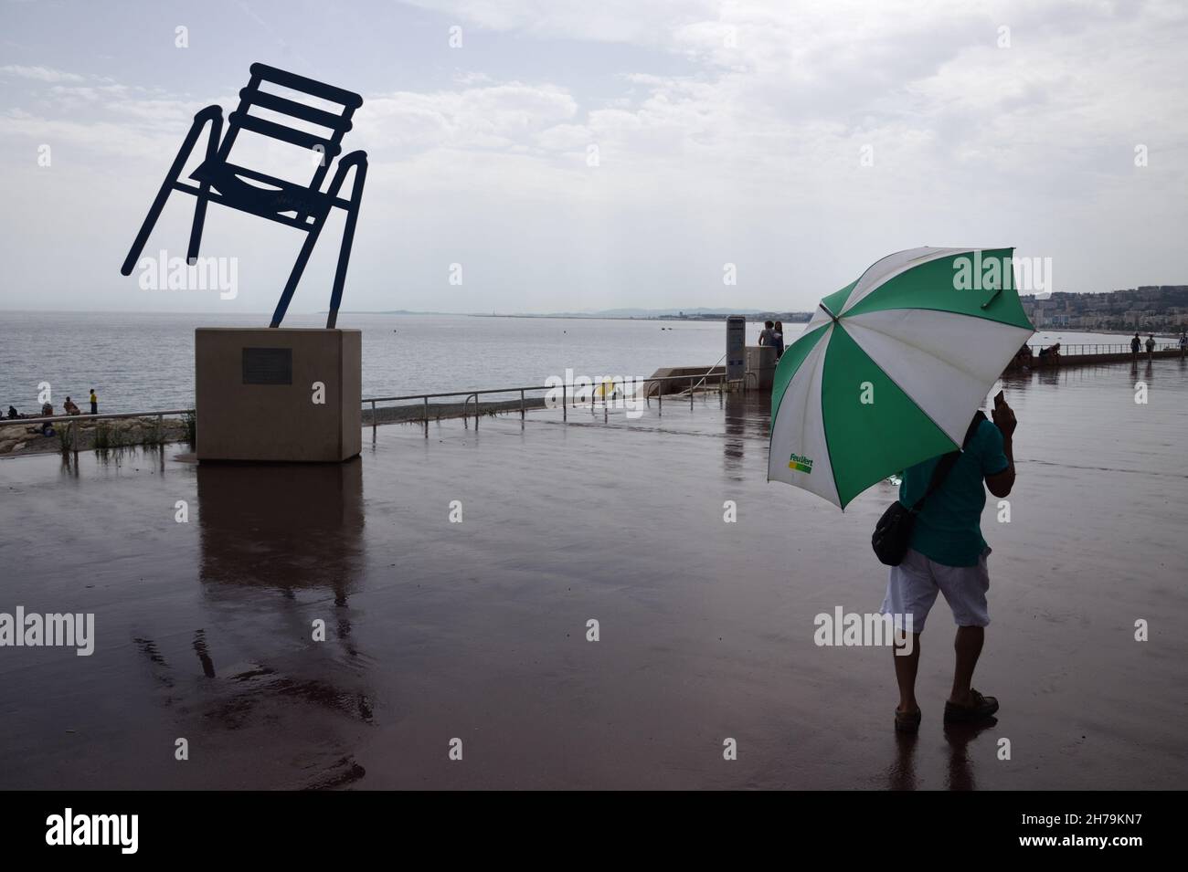 Uomo e ombrello in giornata di pioggia sulla Promenade des Anglais con Big Blue Chair Sculpture di Sabine Geraudie Nice Alpes-Maritimes Francia Foto Stock