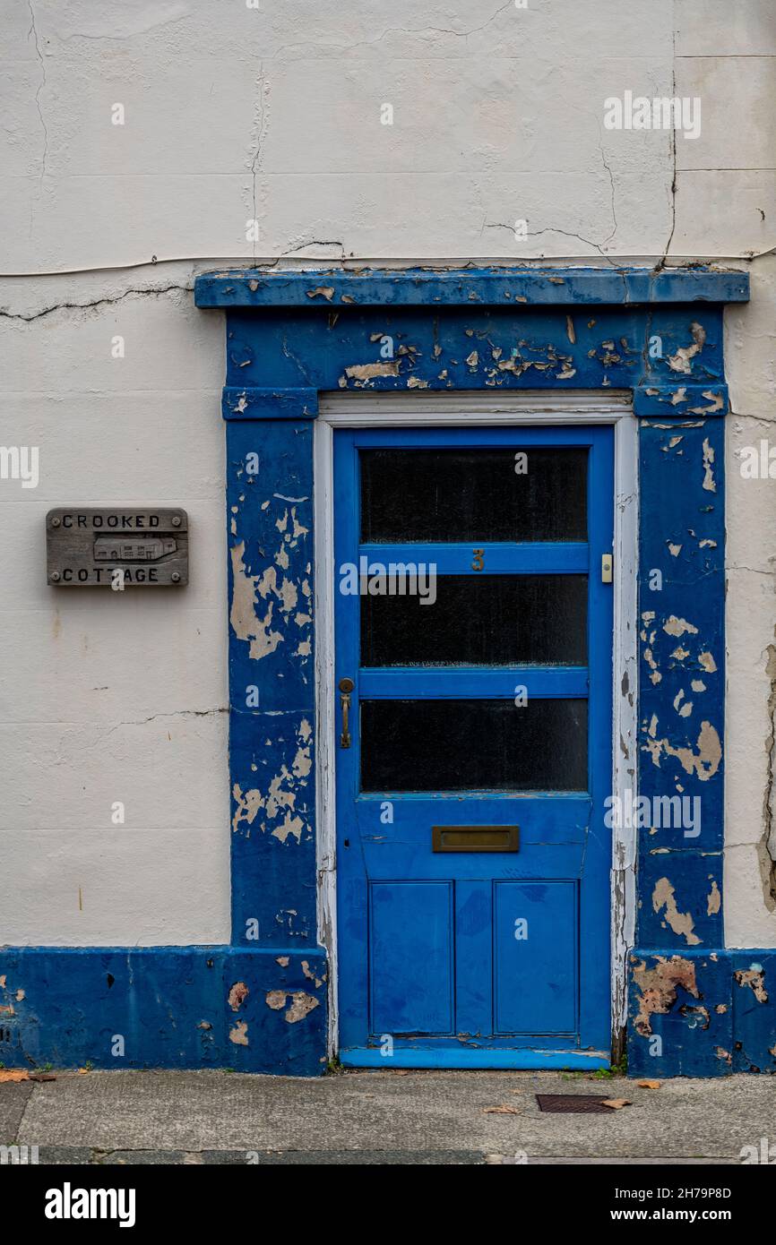 insegna cottage crooked, porta vecchio dilapidated su un cottage dipinto di blu con sfaldatura e peeling vernice, casa nome cottage crooked segno. Foto Stock