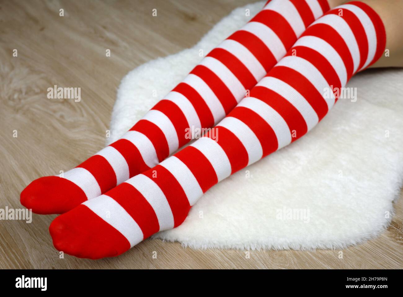 Ragazza in calze di ginocchio di Natale seduta su tappeto di pelliccia bianca su pavimento di legno. Abito femminile per la festa di Capodanno Foto Stock