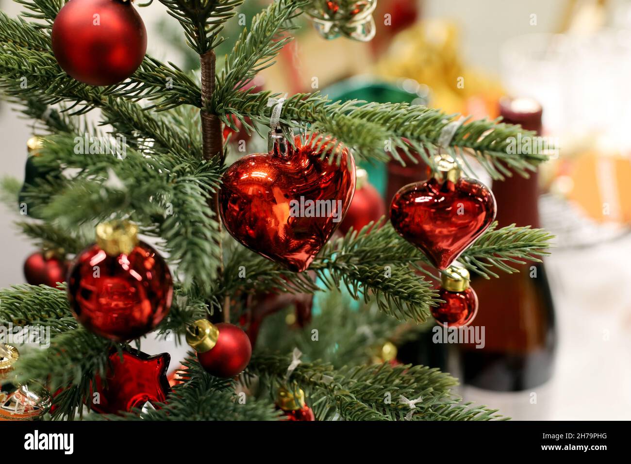 Piccolo albero di Natale con giocattoli rossi su un tavolo con bottiglie di vino. Decorazioni natalizie per la celebrazione di Capodanno Foto Stock
