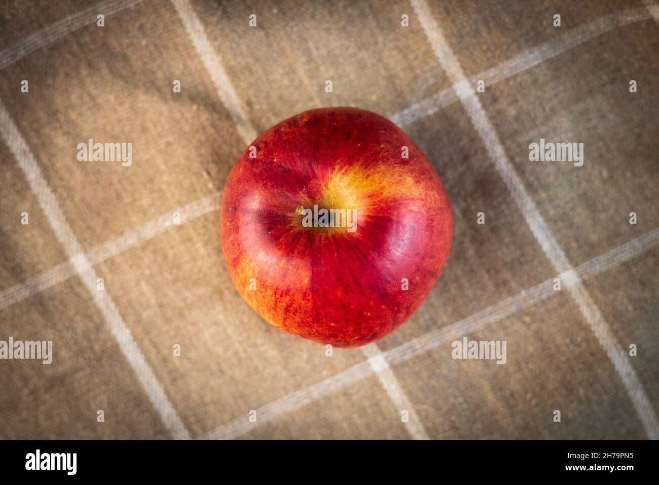 Un'allettante mela d'autunno rossa con una tinta gialla dall'alto. Asciugamano in lino sullo sfondo, marrone chiaro con quadrati bianchi. Una fotografia di un sano l Foto Stock
