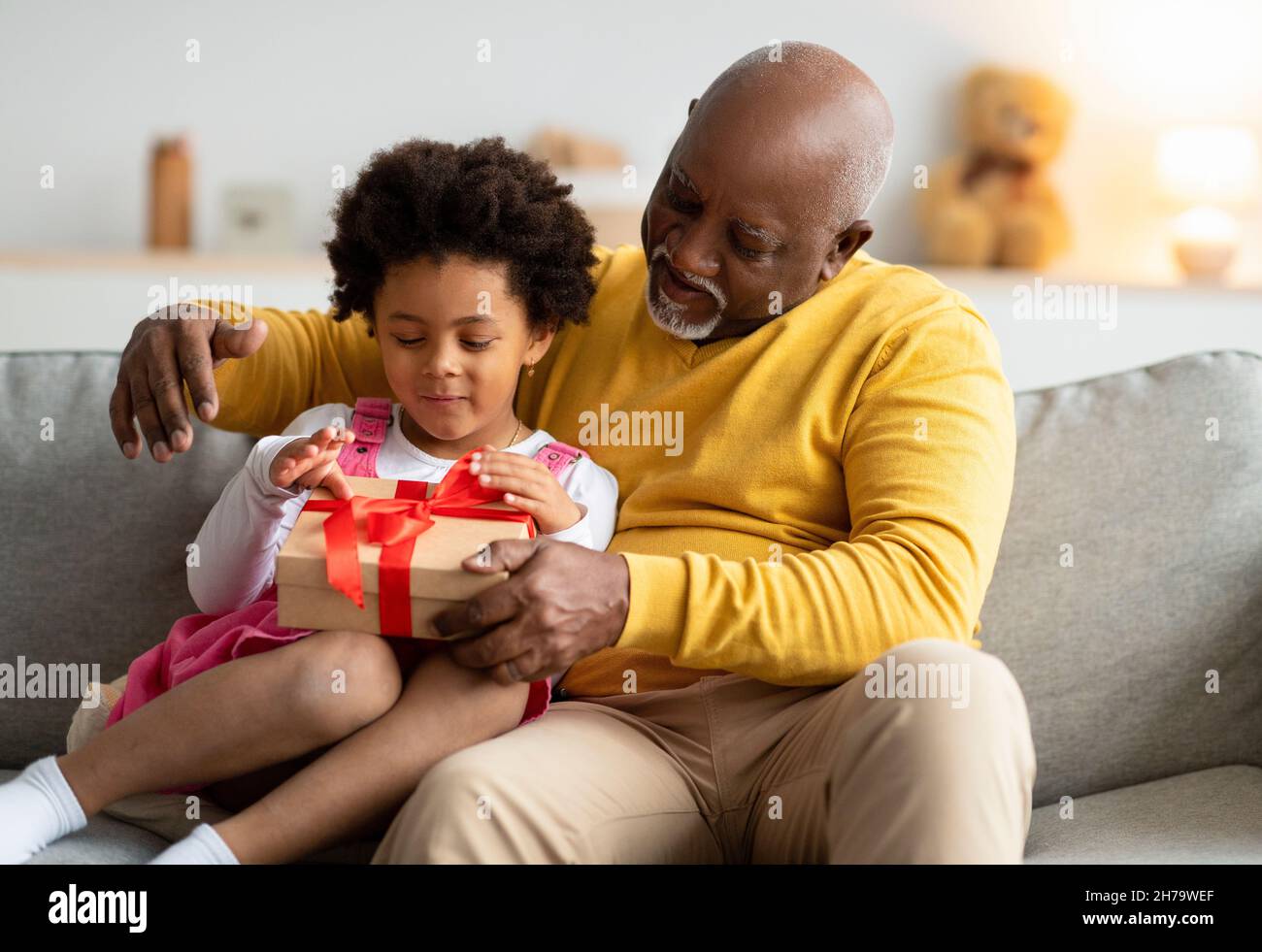 Felice felice carino africano americano prescolare capretto e vecchio uomo aperto compleanno presente in soggiorno Foto Stock