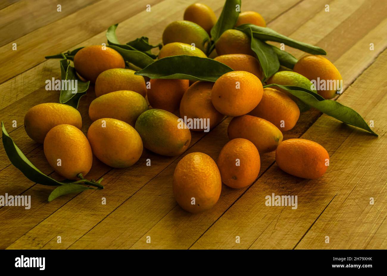 Gruppo di arancio dorato Kumquat - piccoli agrumi tropicali con buccia commestibile, si trovano su un asse di legno Foto Stock